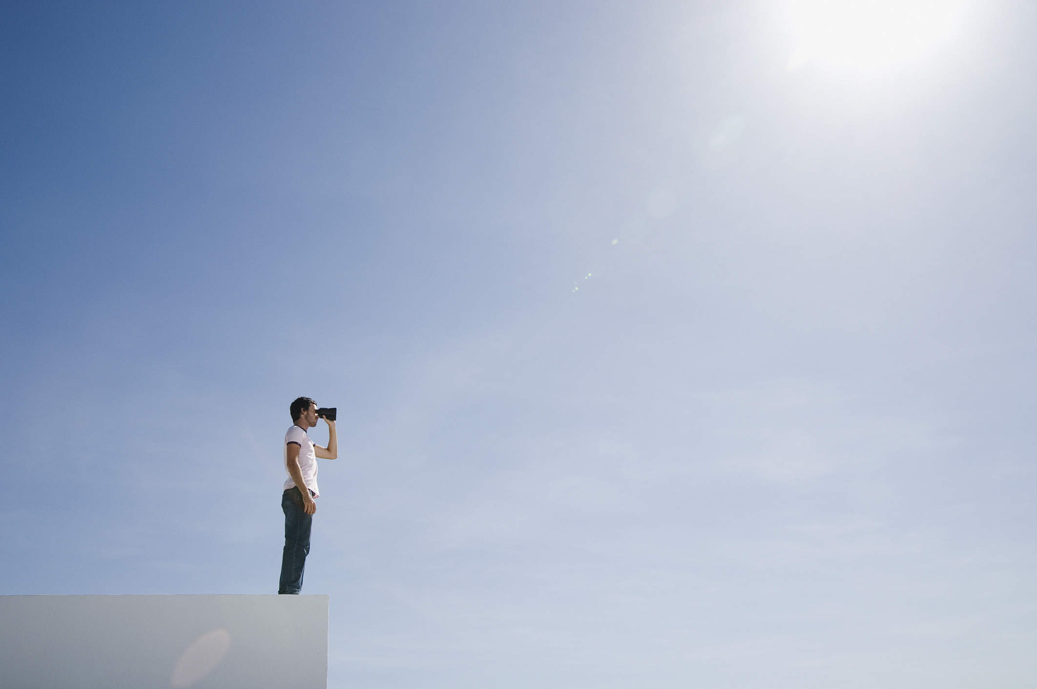 Man on pedestal with binoculars and blue sky outdoors